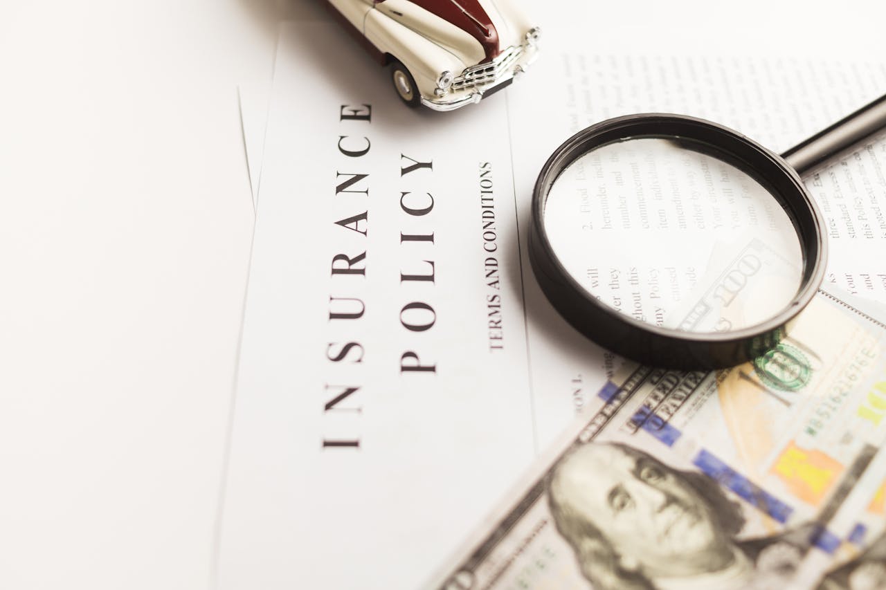 Home Close-up image of an insurance policy with a magnifying glass, money, and toy car.